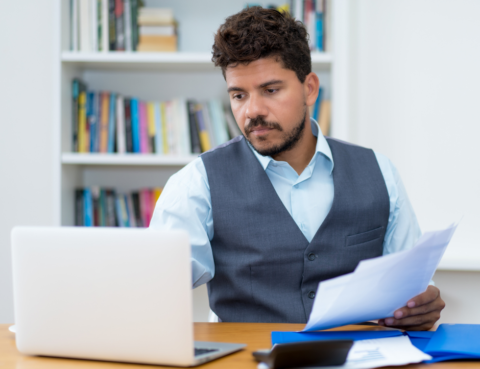 man holding paper working on laptop